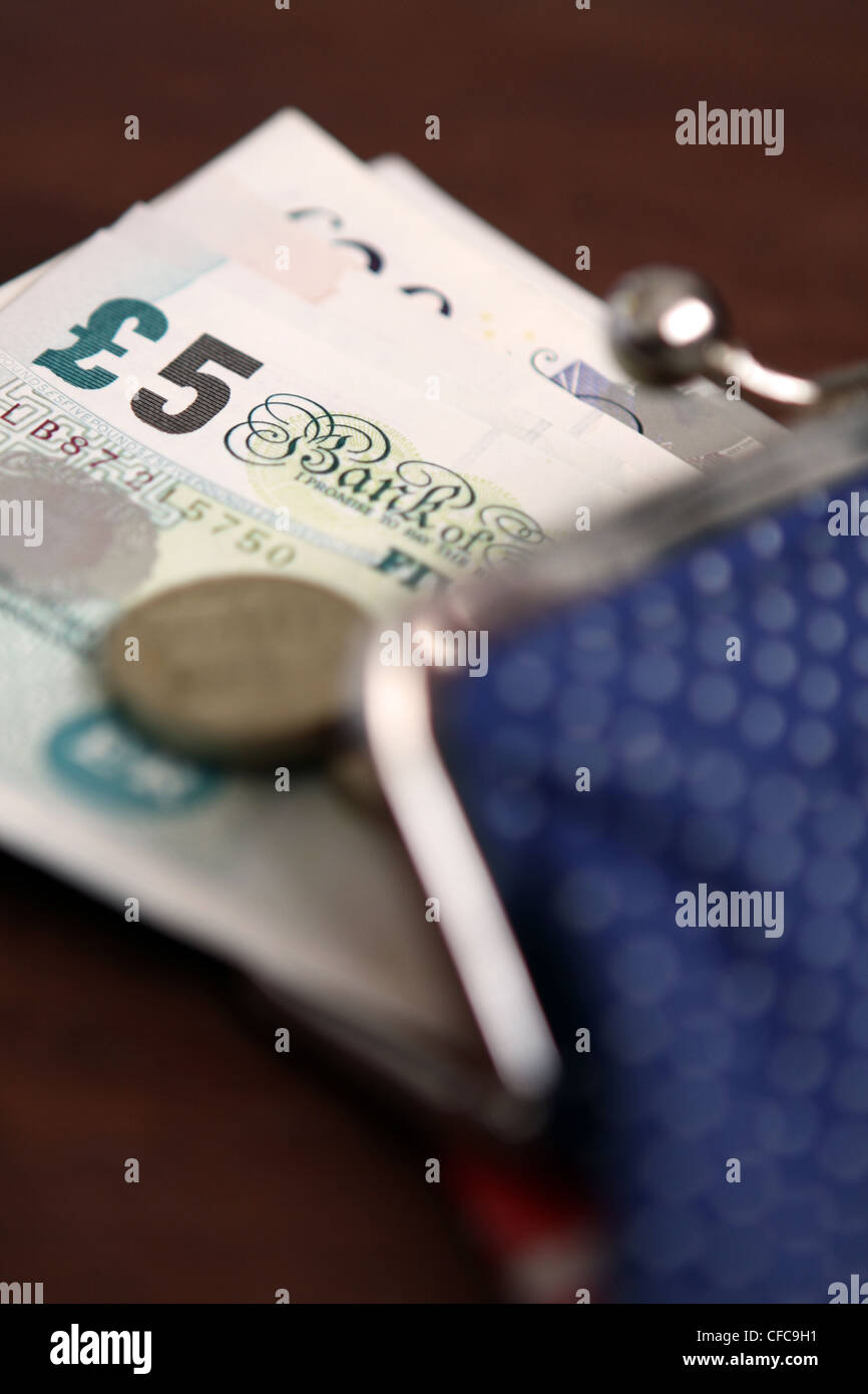 Sterling banconote e monete spuntando fuori da una signora di portamonete aperto Foto Stock