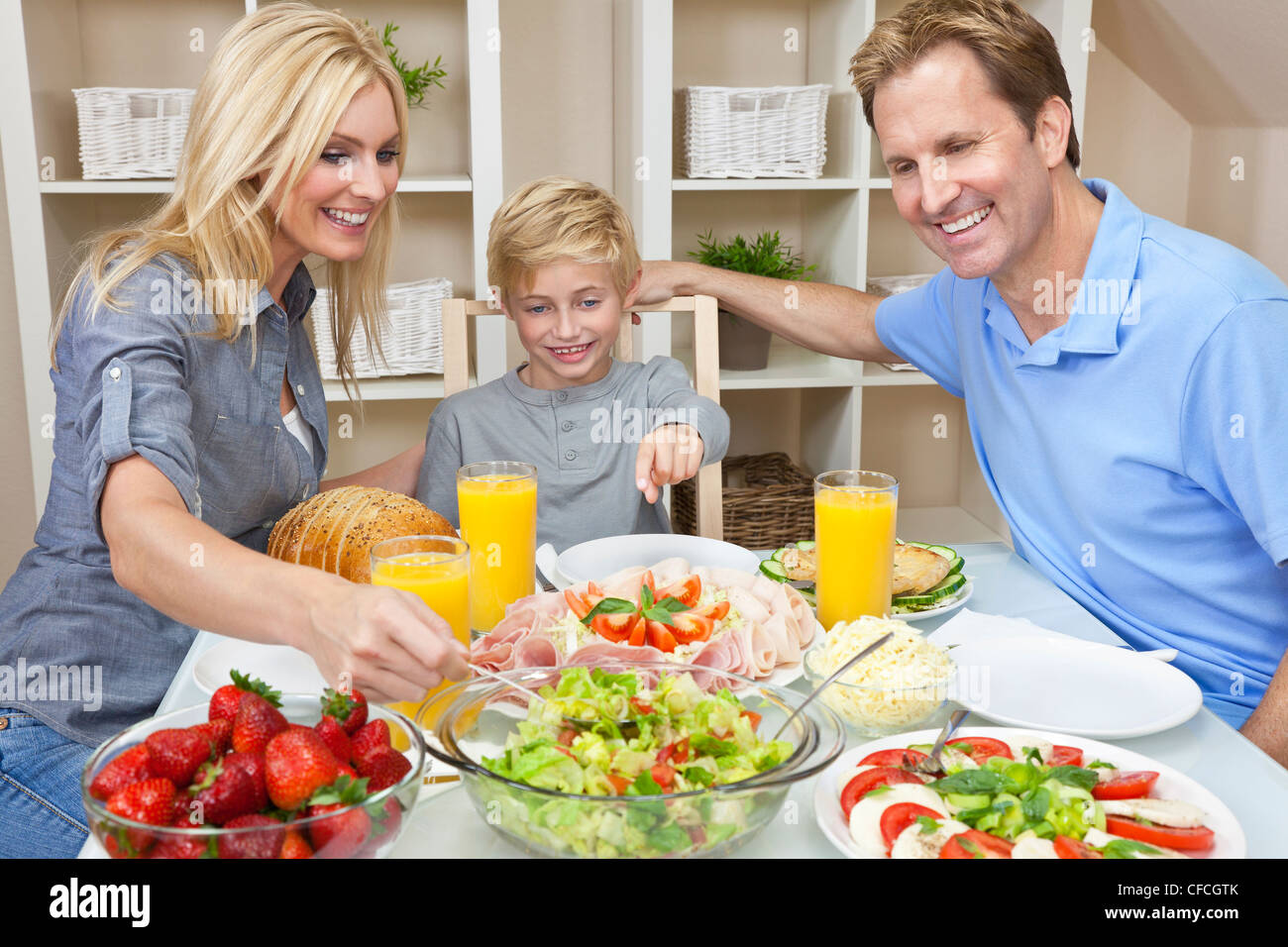 Un attraente felice, sorridente famiglia della madre, padre e figlio di mangiare insalate e cibi sani in un tavolo da pranzo Foto Stock