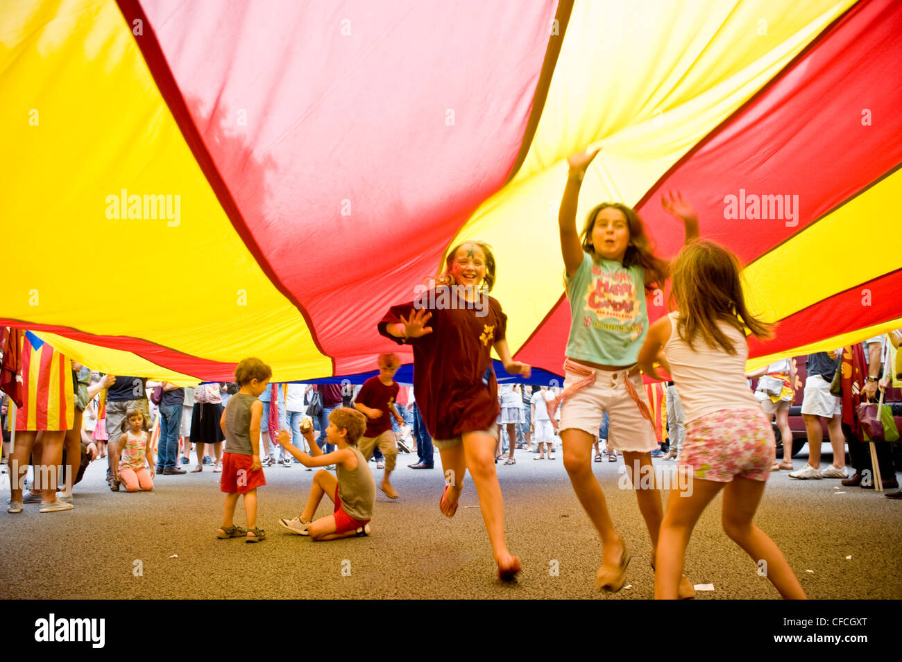 I bambini giocare e divertirsi sotto una grande bandiera catalana durante il catalano della Giornata Nazionale di Barcellona. Foto Stock