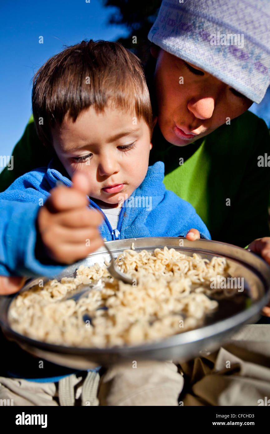 Un ragazzo si siede sul suo madri giro mentre mangiano gli spaghetti nel backcountry. Essi sono accampati presso Squaw Pass. Foto Stock