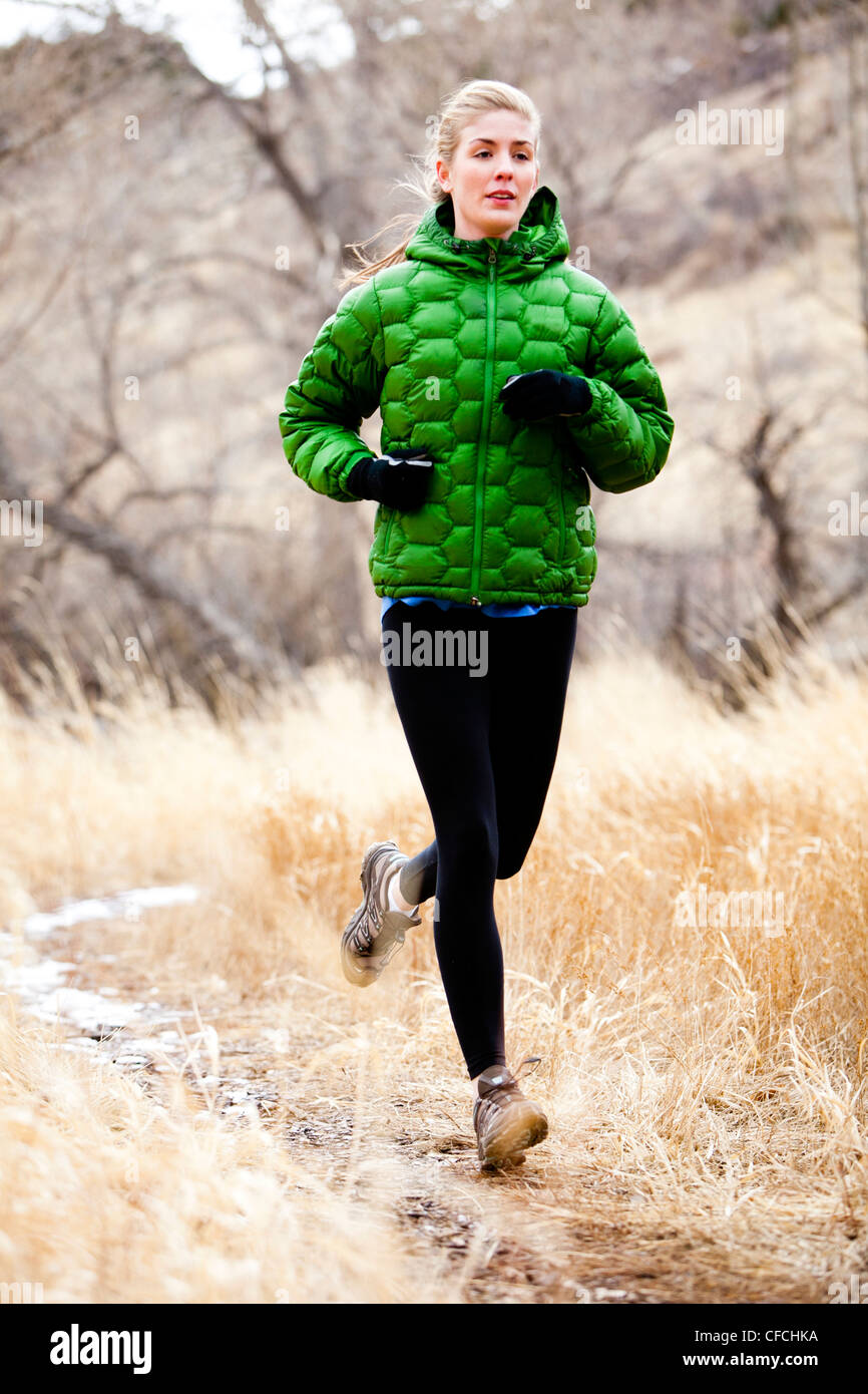 Una giovane donna corre un sentiero verso il basso attraverso l'erba Morta appena a nord di Dixon serbatoio, in un freddo giorno di un verde down jacket. Foto Stock