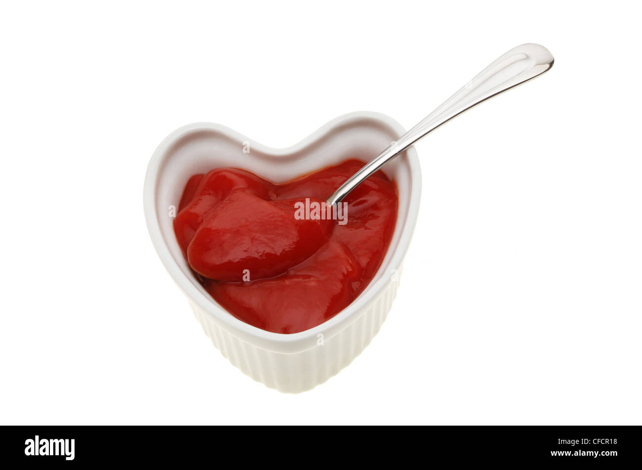 Il ketchup in un cuore ramekin sagomato con un cucchiaio isolata contro bianco Foto Stock