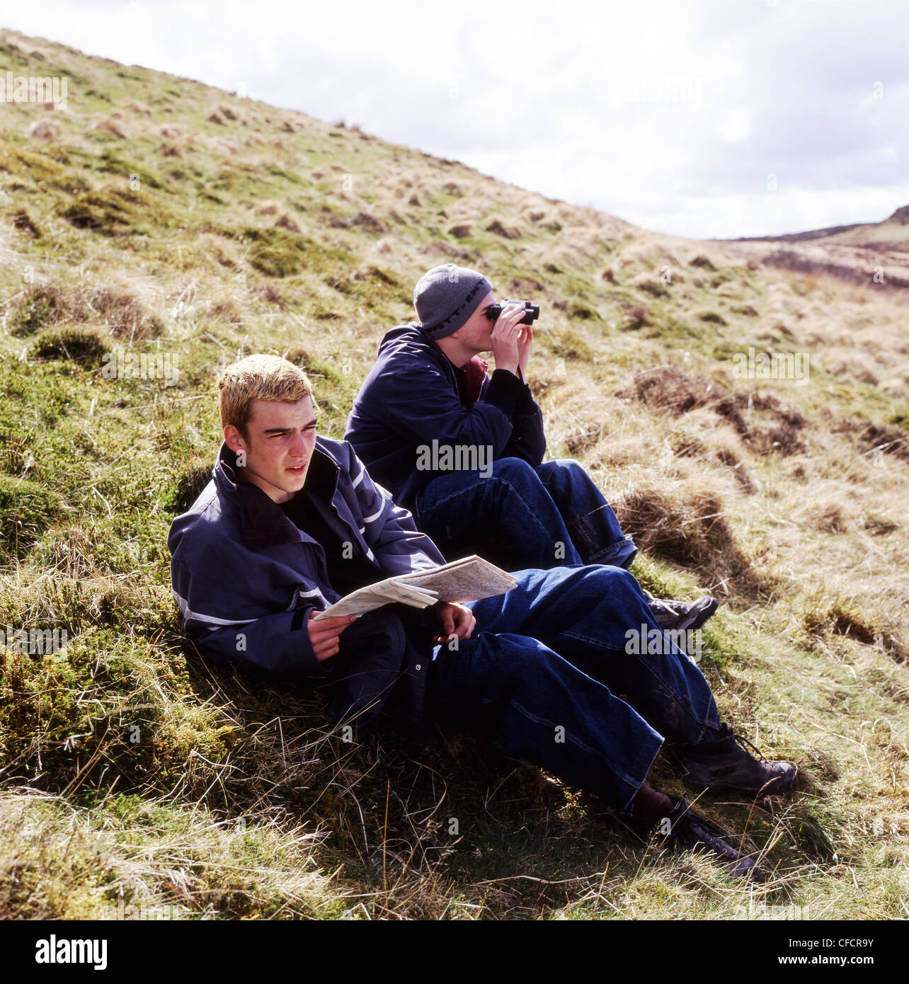 I giovani escursionisti uomini guardando la mappa e utilizzando il binocolo localizzare la loro posizione su una collina gallese in Galles Carmarthenshire UK KATHY DEWITT Foto Stock