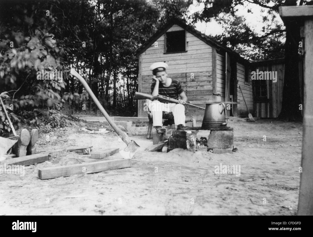 Ragazzo seduto con un fucile fuori homestead Casa Marina fuoco uniforme bollitore 1920s 1930 onirica Foto Stock