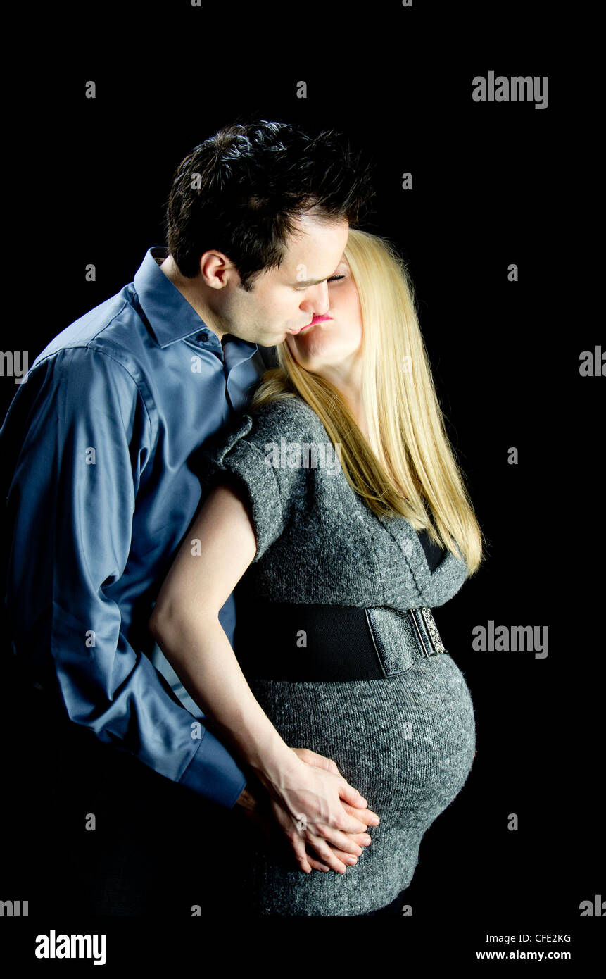 Una immagine di maternità di un giovane, baciare, contro una chiave di basso, sfondo nero. Foto Stock