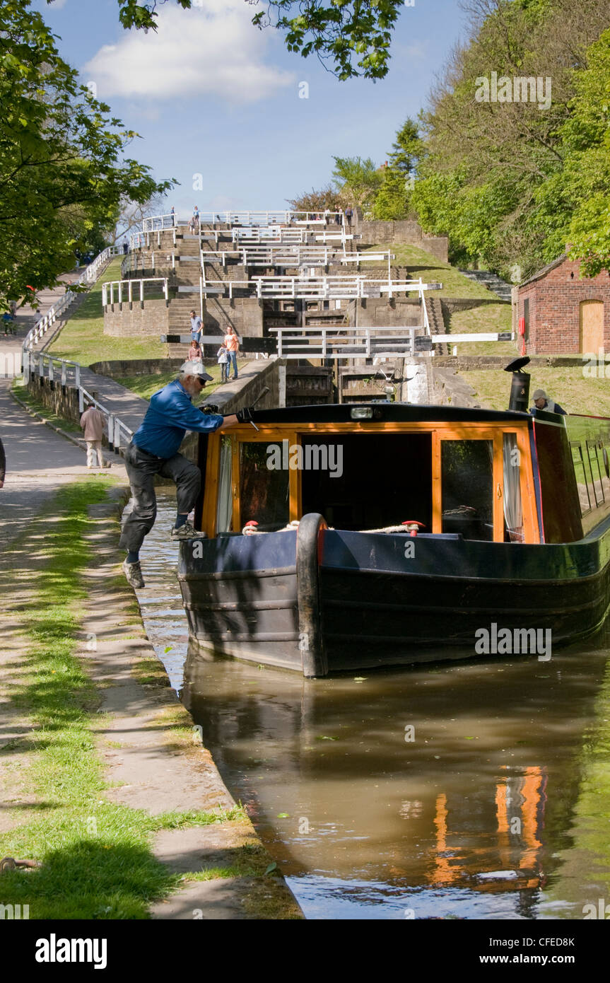 Uomo di saltare a bordo narrowboat da alzaia, dopo aver viaggiato attraverso la paesaggistica cinque serrature aumento - Leeds Liverpool Canal, West Yorkshire, Inghilterra, Regno Unito. Foto Stock