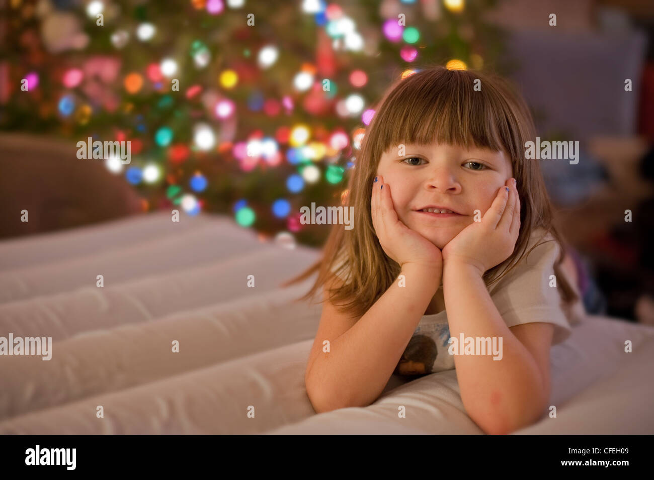 Carino 5 anno vecchia ragazza in posa davanti un colorato albero di natale e le luci. Foto Stock