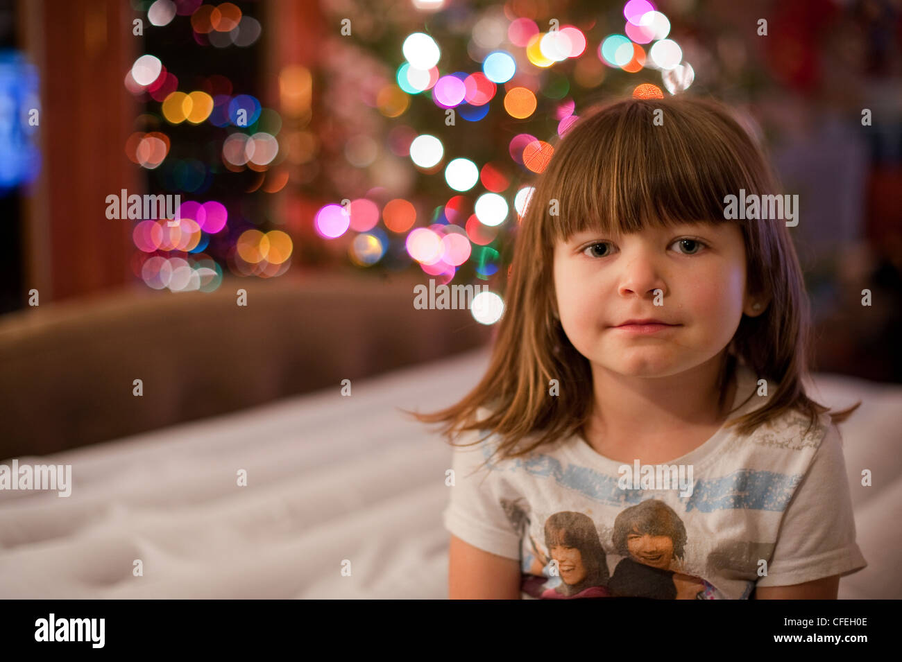 Carino 5 anno vecchia ragazza in posa davanti un colorato albero di natale e le luci. Foto Stock