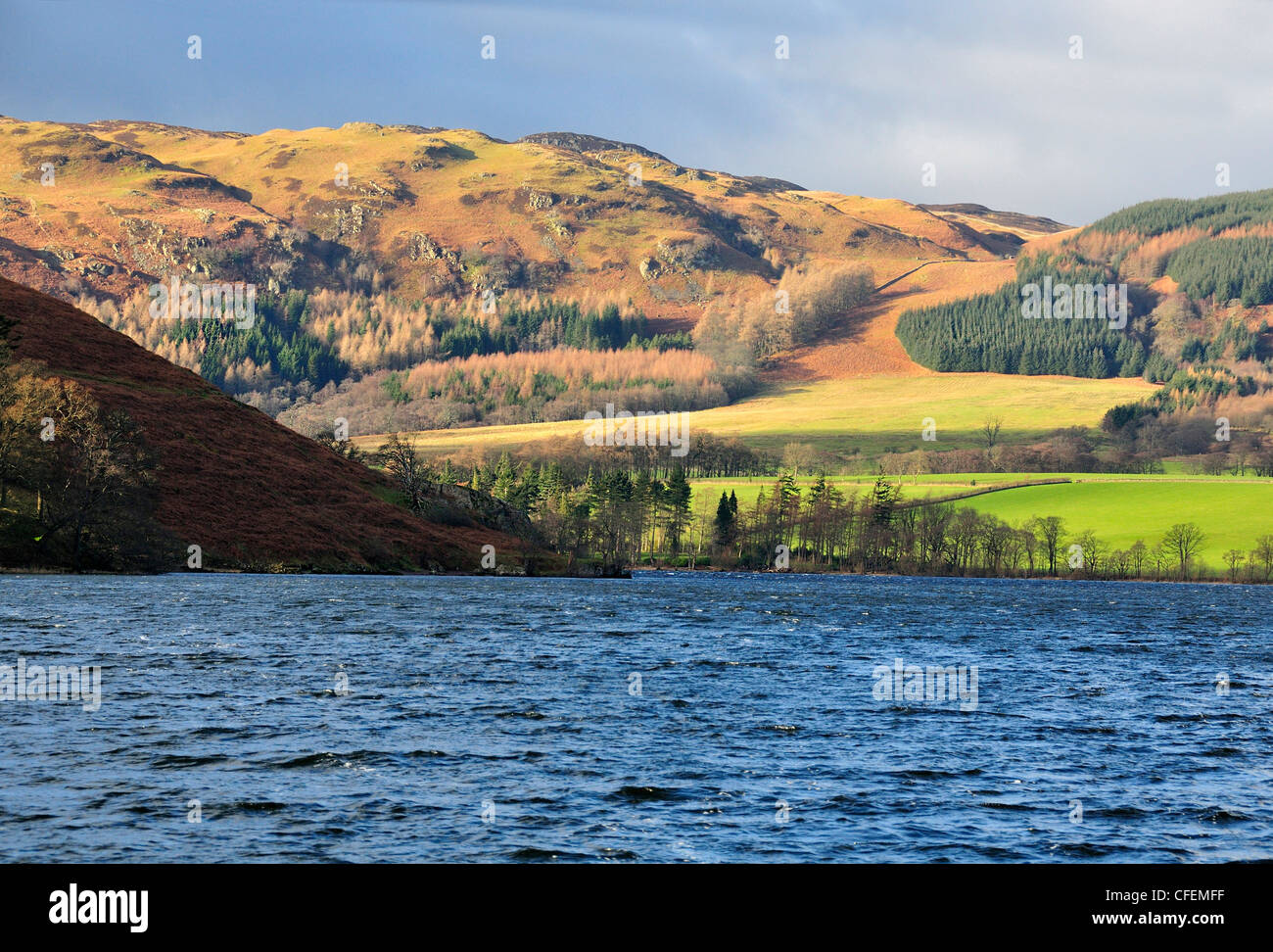 Preso dal lago Ullswater, Cumbria, Inghilterra con alberi di luce del sole sulla circostante fells durante il periodo invernale Foto Stock