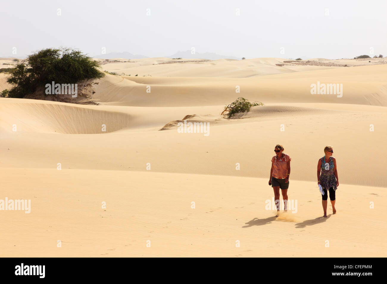 Vista di due donne turisti camminare a piedi scalzi sul caldo vuoto dune di sabbia del deserto. Deserto de Viana, Boa Vista, Isole di Capo Verde. Foto Stock