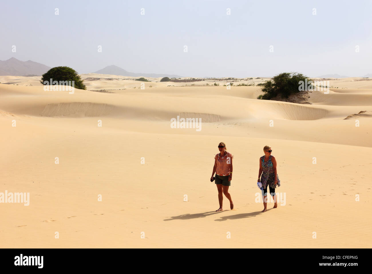 Vista di due donne turisti camminare a piedi scalzi sul caldo vuoto dune di sabbia del deserto. Deserto de Viana, Boa Vista, Isole di Capo Verde, Africa Foto Stock