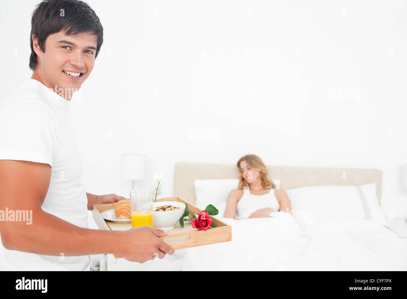 Uomo sorridente come egli porta la donna colazione, la donna dorme Foto Stock