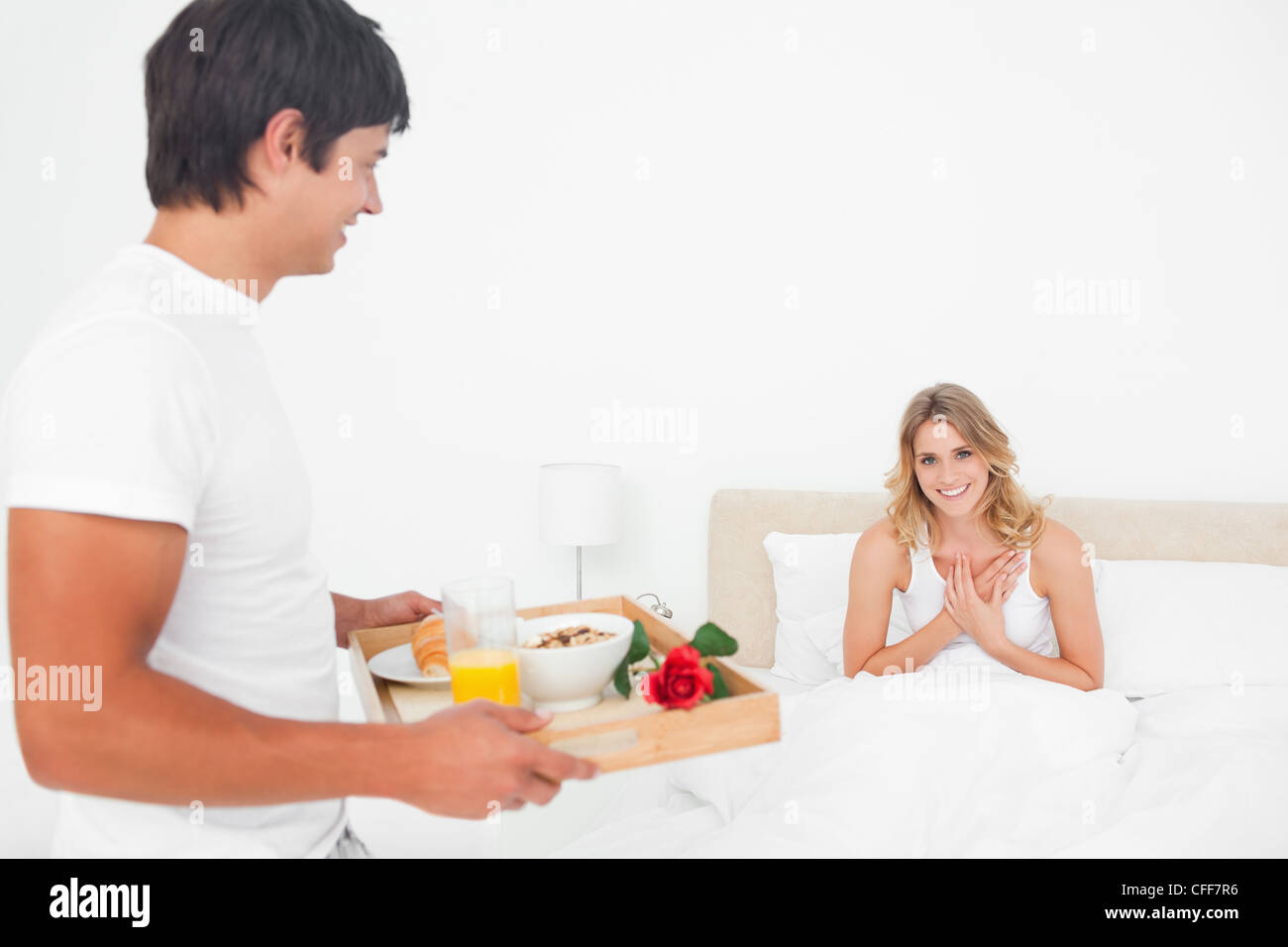 La donna mostra gratitudine e sorrisi come l'uomo porta la sua colazione a letto Foto Stock