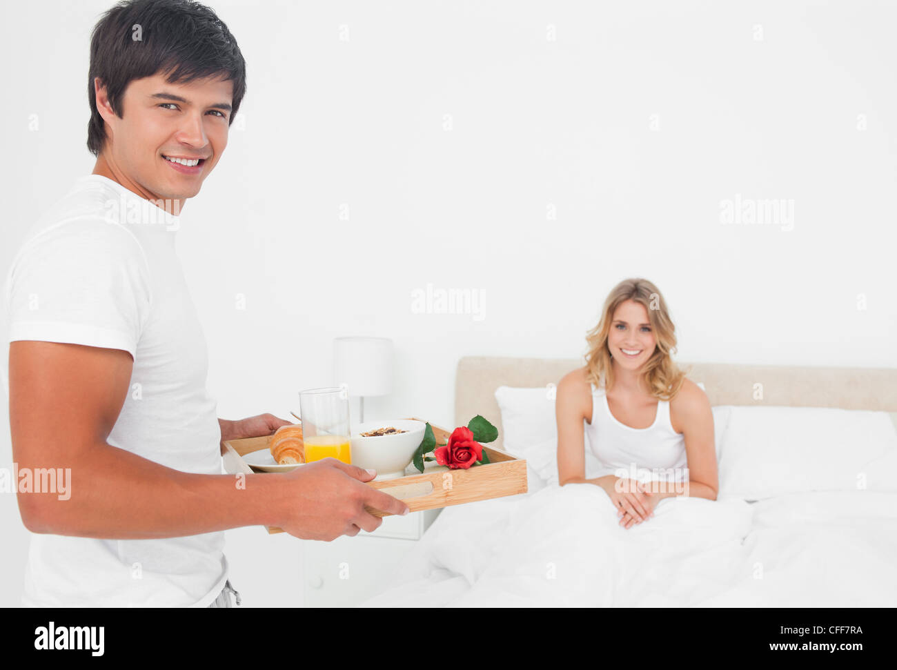 L uomo e la donna sono entrambi di sorridere quando egli porta la sua colazione a letto Foto Stock