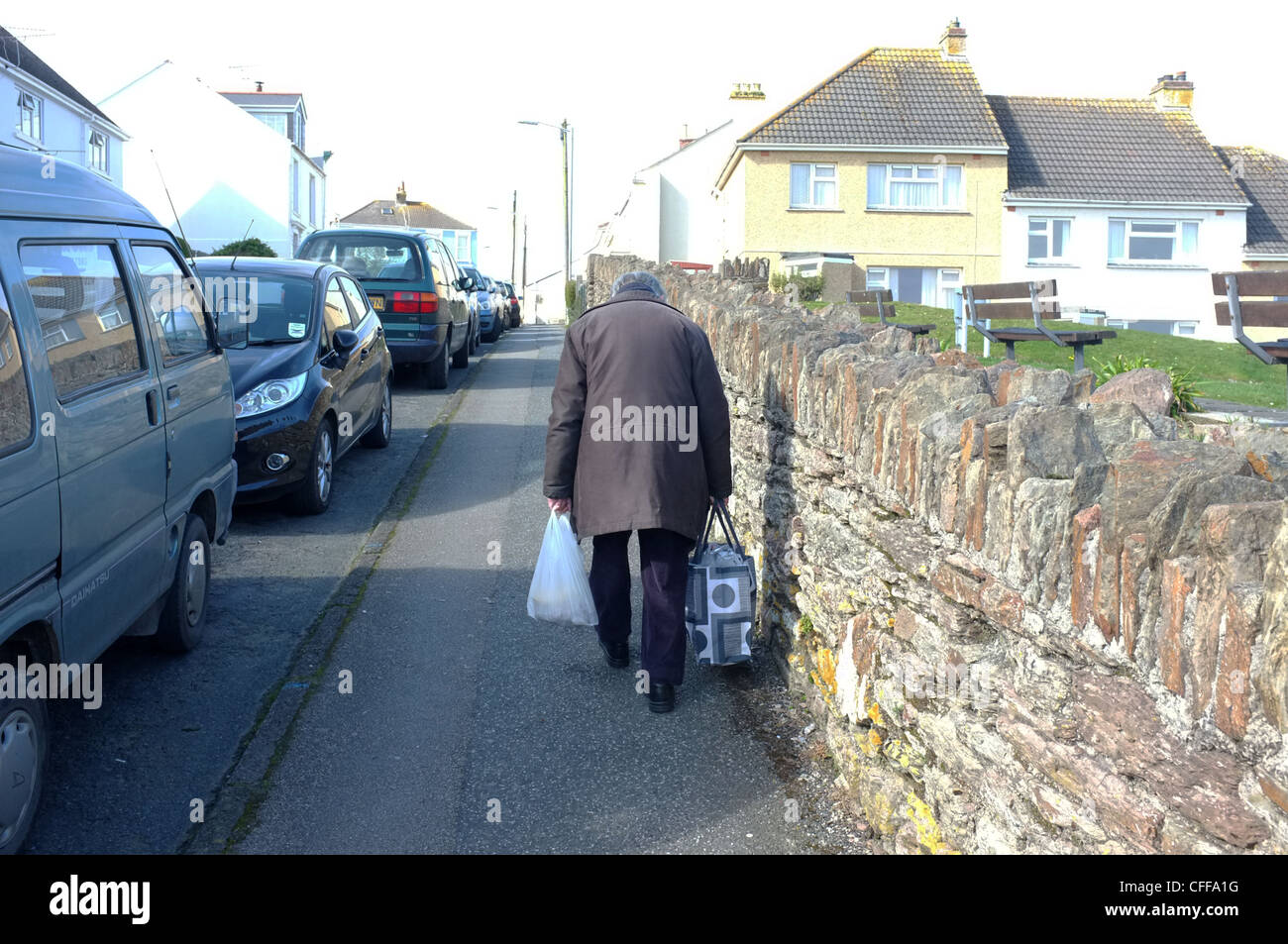Un vecchio uomo cammina su una ripida collina con il suo shopping a Falmouth, Regno Unito Foto Stock
