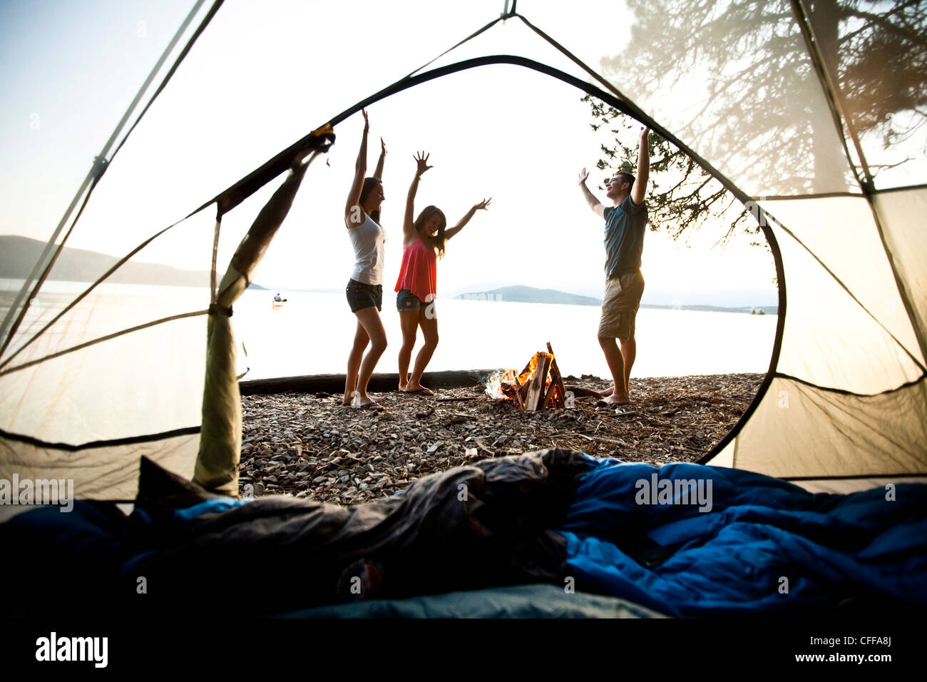 Tre giovani adulti sorridente e ballando intorno ad un fuoco di campo su un campeggio e viaggio in kayak sul lago in Idaho. Foto Stock