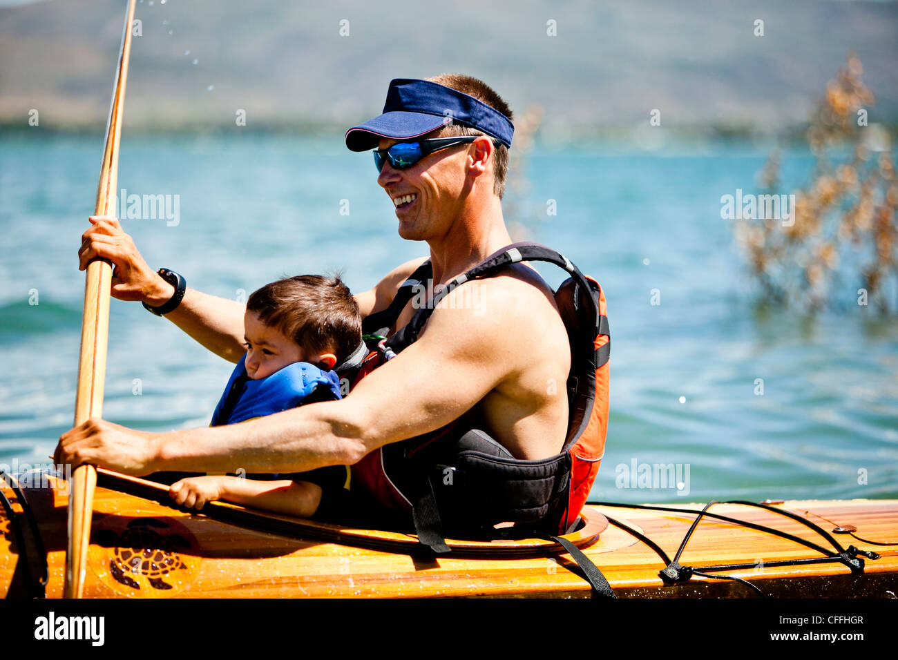 Un uomo pagaie in legno kayak con un 3 anno vecchio ragazzo nel suo giro. Foto Stock