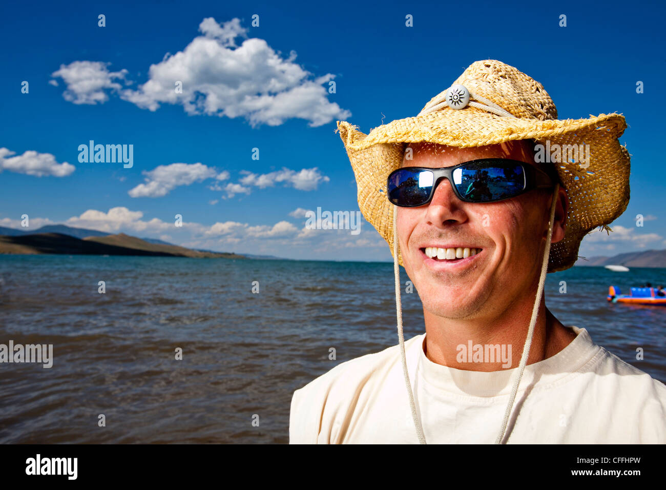 Un uomo sorride in un cappello di paglia come egli si distingue per un ritratto sulle sponde del Bear Lake, Utah. Foto Stock