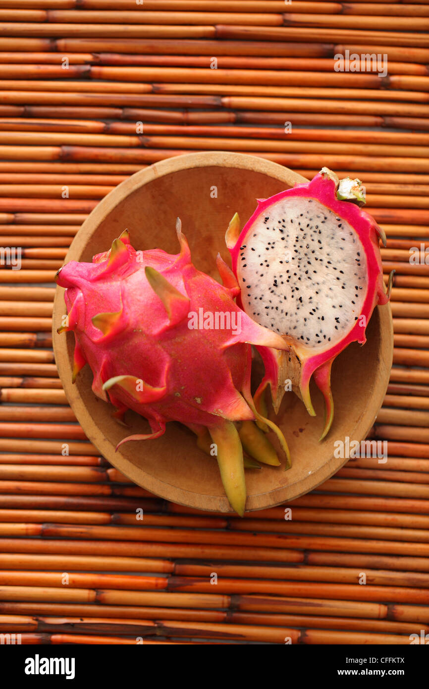 Intero e metà drago frutto nella ciotola di legno su sfondo di bambù Foto Stock