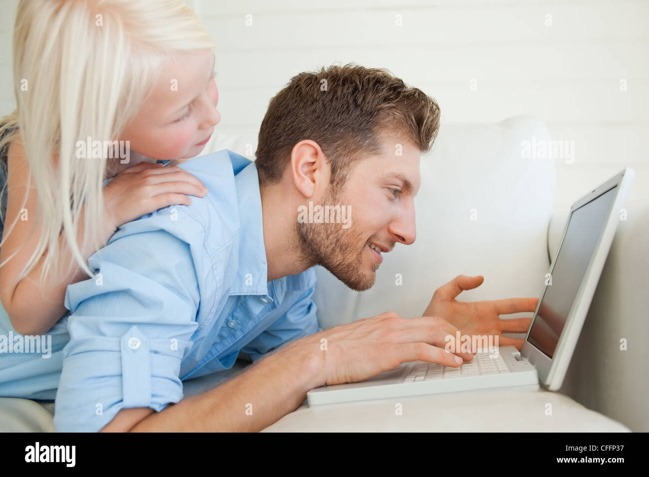 Un uomo disteso sul lettino con il suo computer portatile come sua figlia si trova in cima a lui Foto Stock