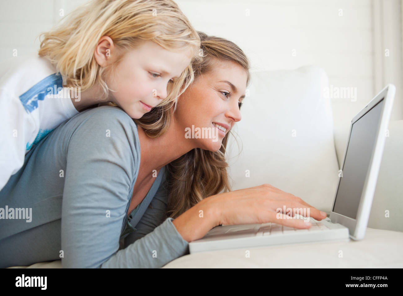 Una donna giace sul lettino con il suo computer portatile come sua figlia si trova sulla parte superiore della sua Foto Stock