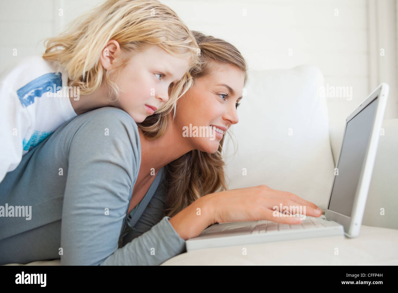 Una donna con il suo computer portatile sdraiato sul lettino sorrisi come sua figlia si trova sul suo Foto Stock