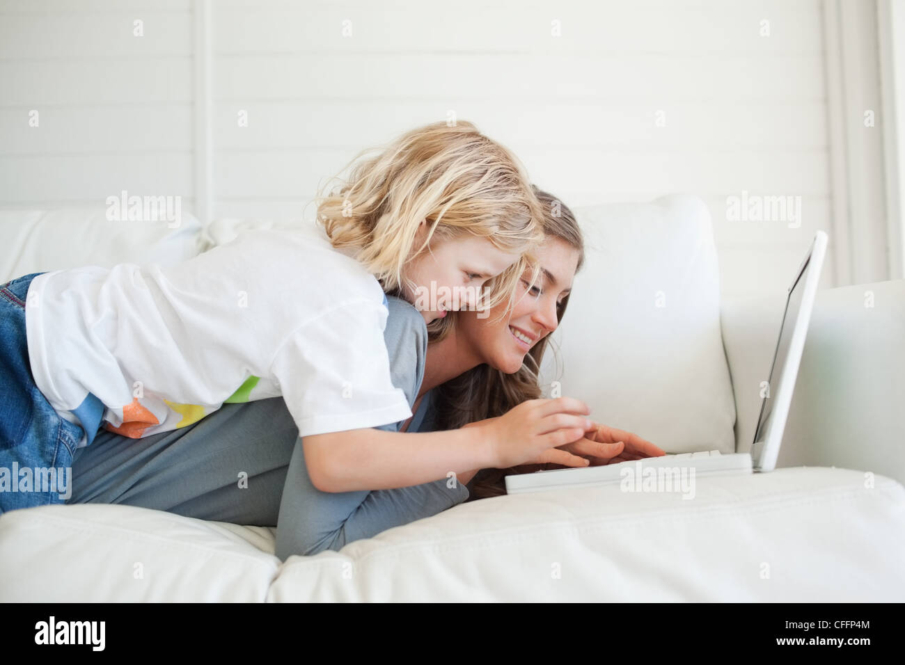 La madre si trova sul lettino usando il suo computer portatile come il ragazzo cerca di aiutare Foto Stock