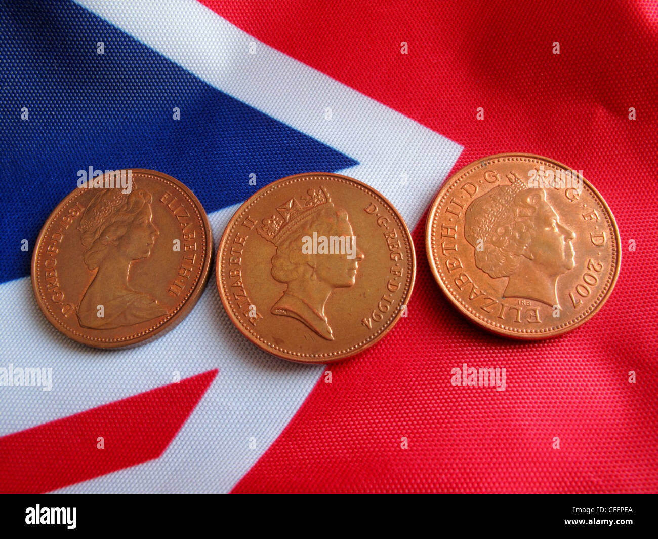 Tre monete di rame set contro un union jack flag , che mostra il Queens Head dalla sua giovinezza per il presente. Foto Stock