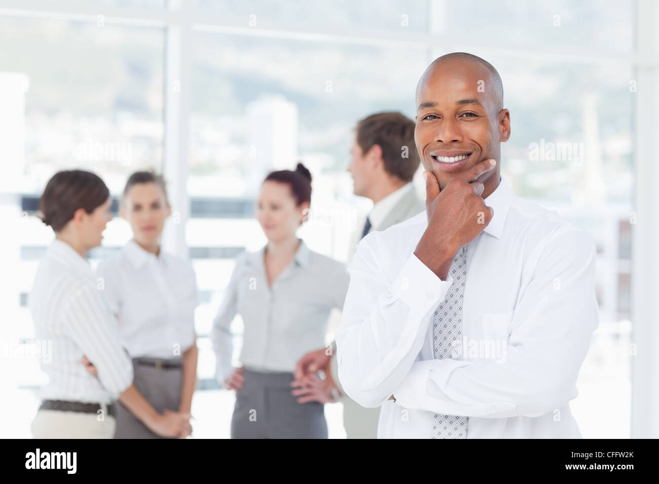 Sorridente venditore in pensatori pongono con colleghi dietro di lui Foto Stock