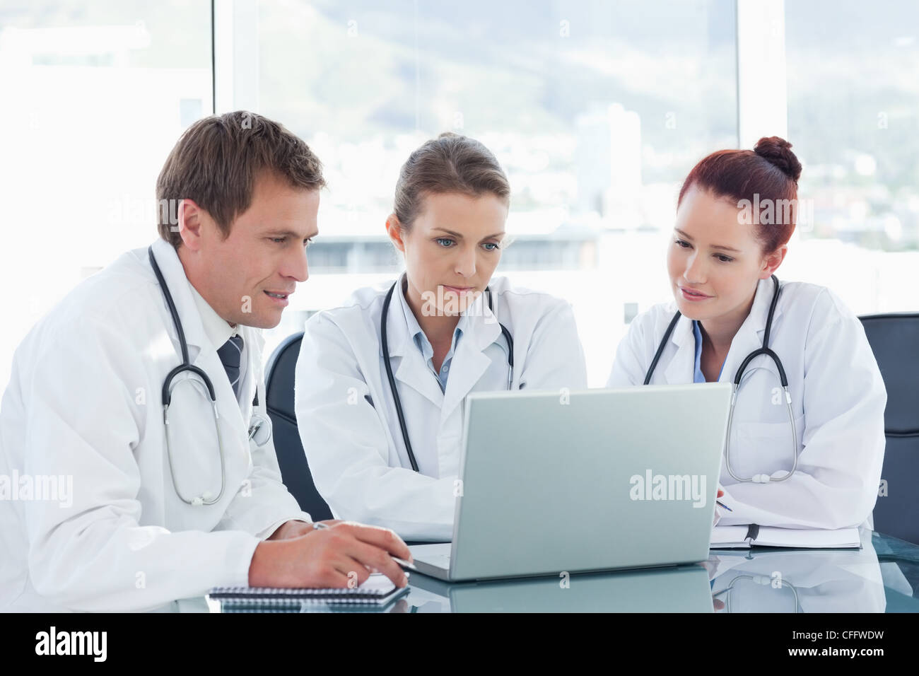 Tre medici con i notebook seduti a un tavolo Foto Stock