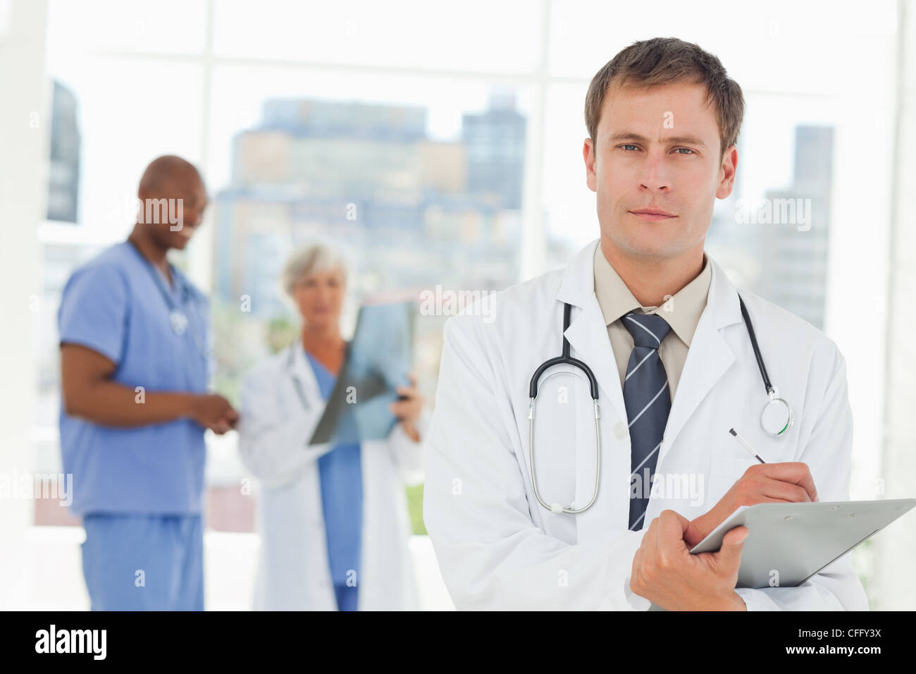 Medico con appunti e colleghi dietro di lui Foto Stock