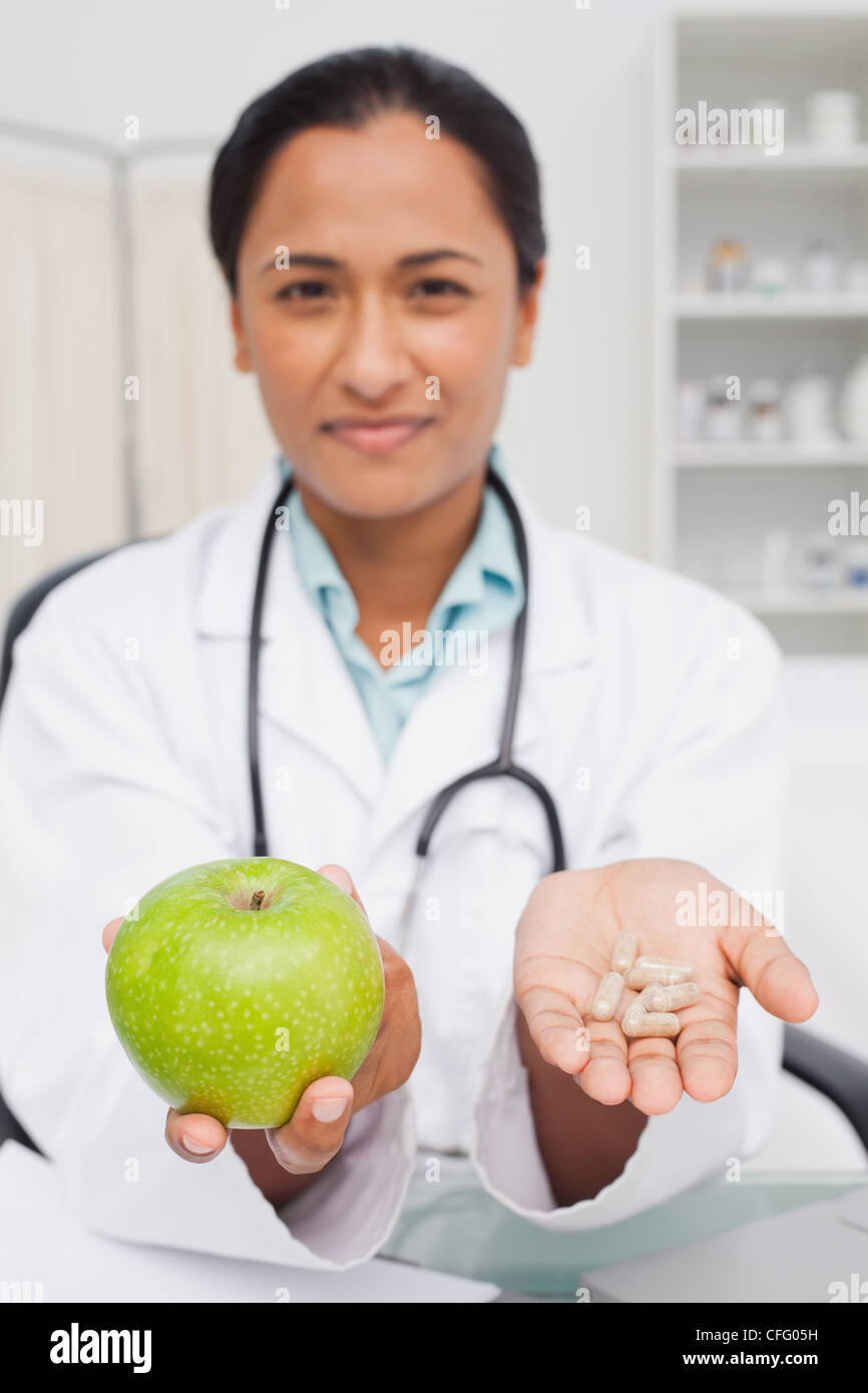 Rilassata medico tenendo una mela verde e vitamine Foto Stock