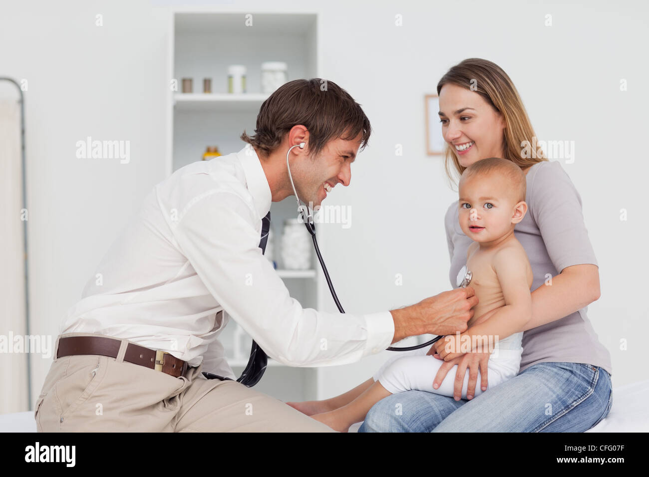 Madre sorridente mentre tiene il suo bambino mentre il medico è tenuto il suo battito cardiaco Foto Stock