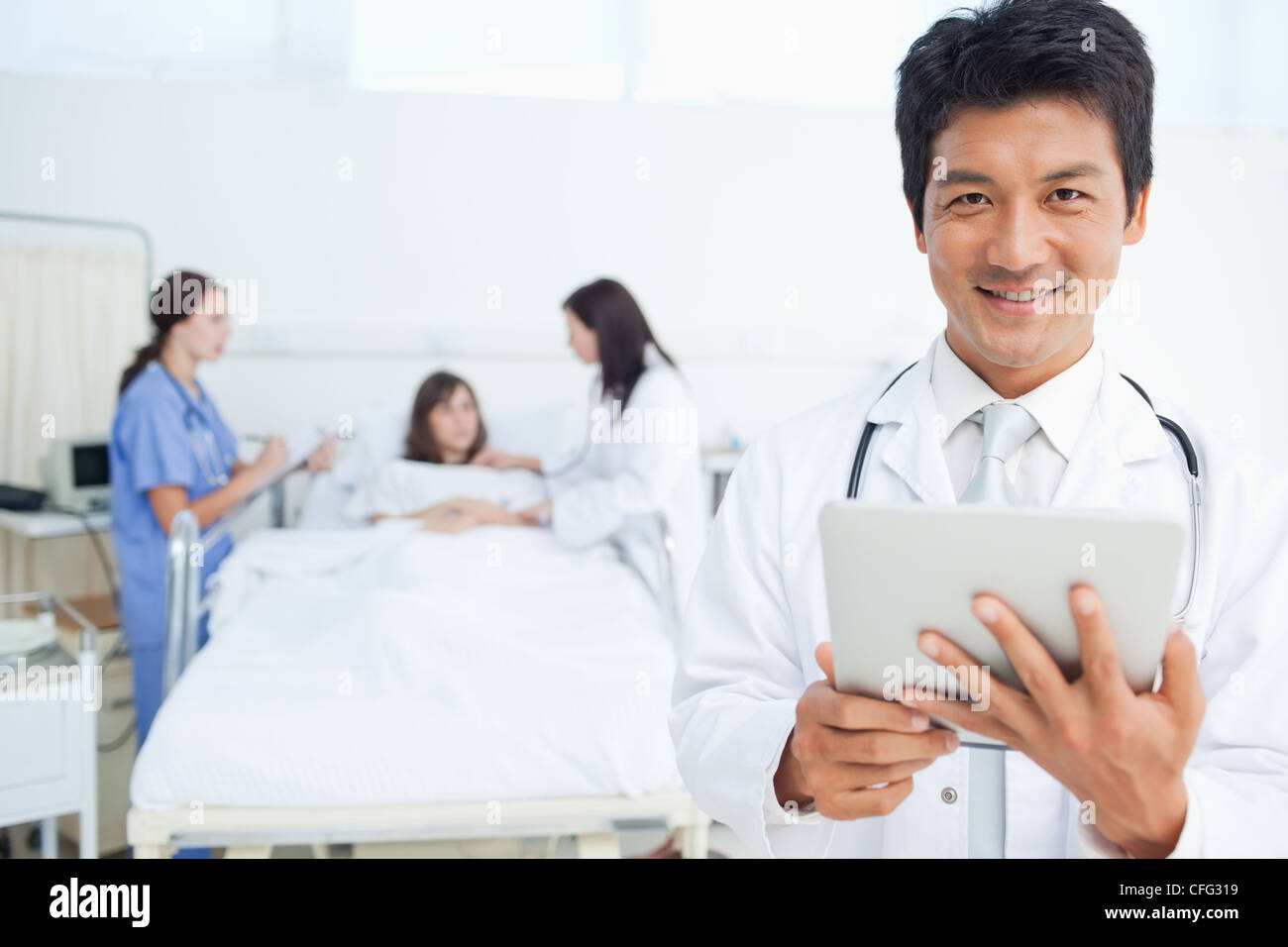 Medico guardando avanti tenendo un tablet come i suoi colleghi il trattamento di un paziente Foto Stock