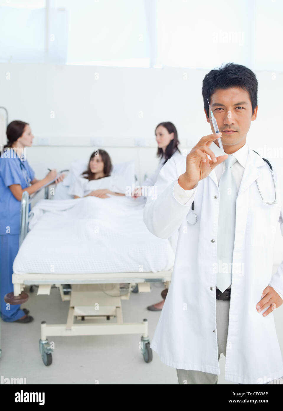 Medico tenendo una siringa davanti a lui e ai suoi colleghi il trattamento di un paziente Foto Stock