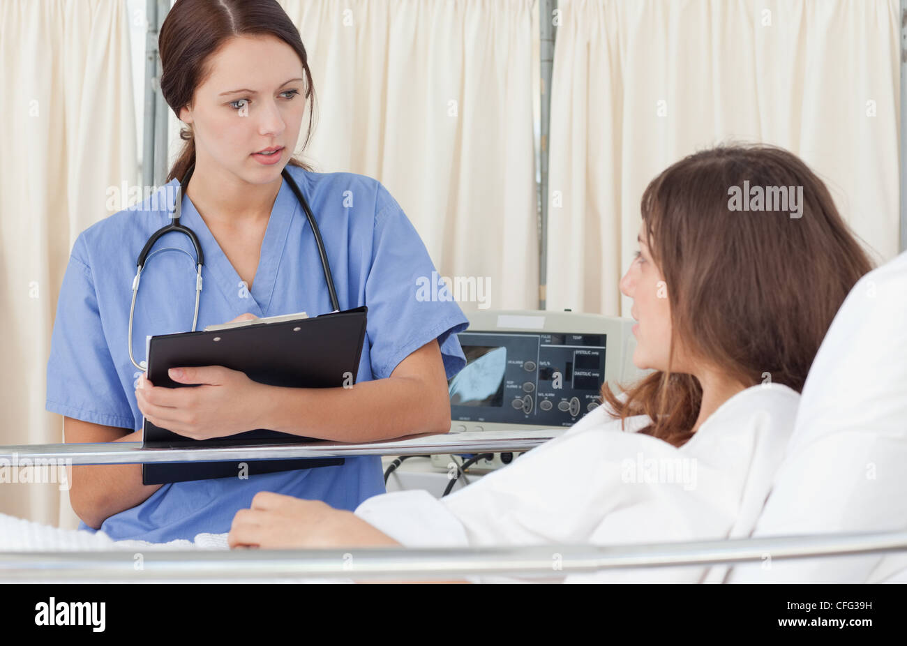 L'infermiera tenendo un clipboard mentre discute con un paziente Foto Stock