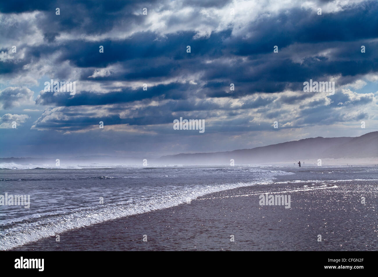 Un buio e minaccioso storm rotoli in oltre una vasta spiaggia con la bassa marea. Foto Stock