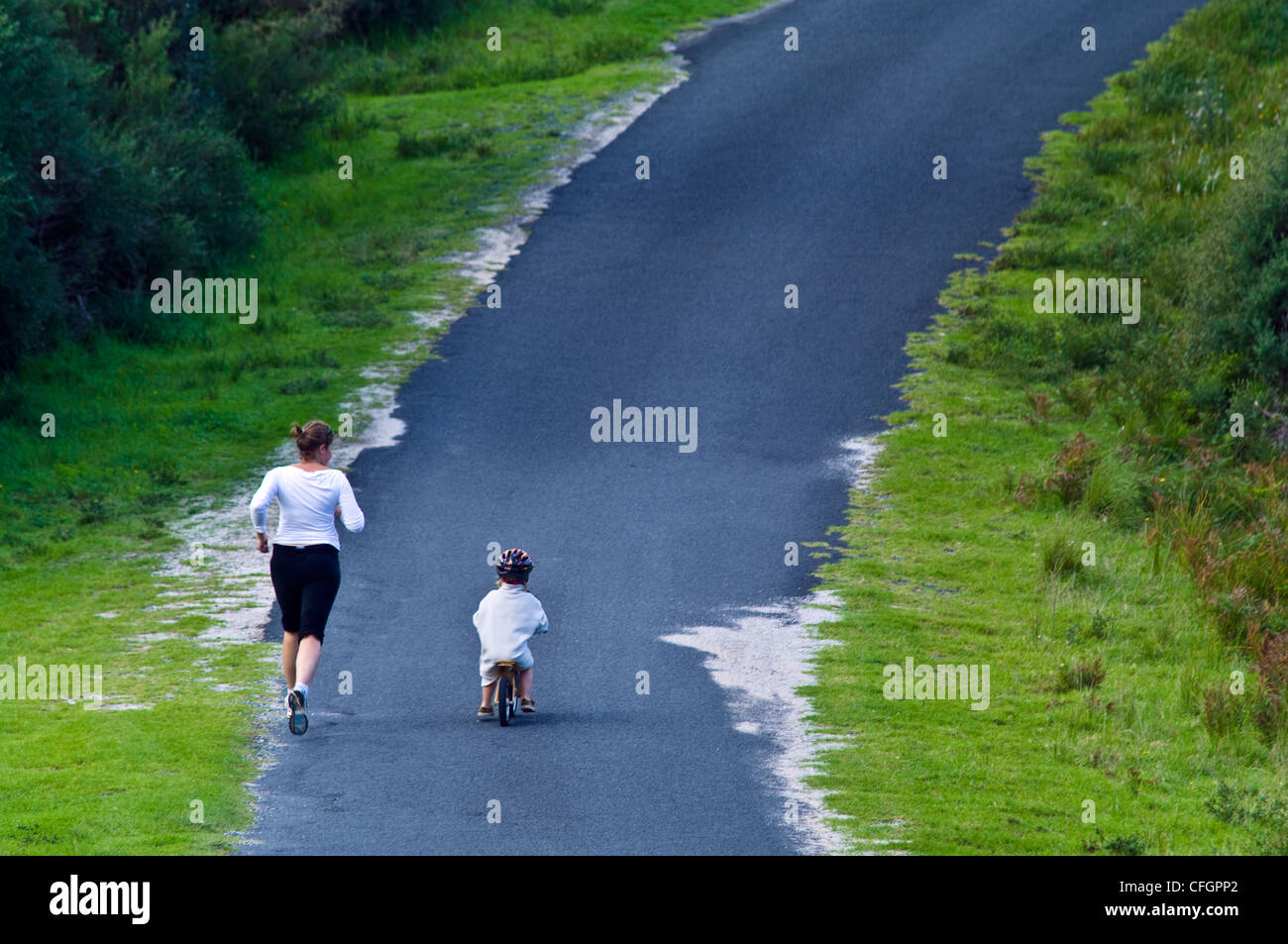 Una madre corre a fianco di suo figlio a cavallo di un equilibrio bici giù per una ripida collina. Foto Stock