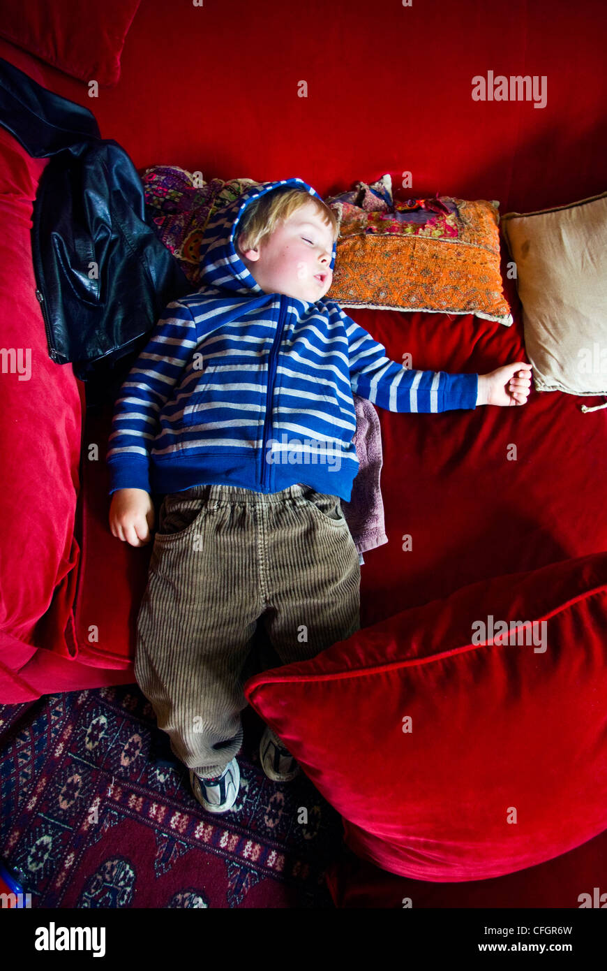Un piccolo ragazzo di addormentarsi sul rosso brillante divani di velluto dei cuscini. Foto Stock