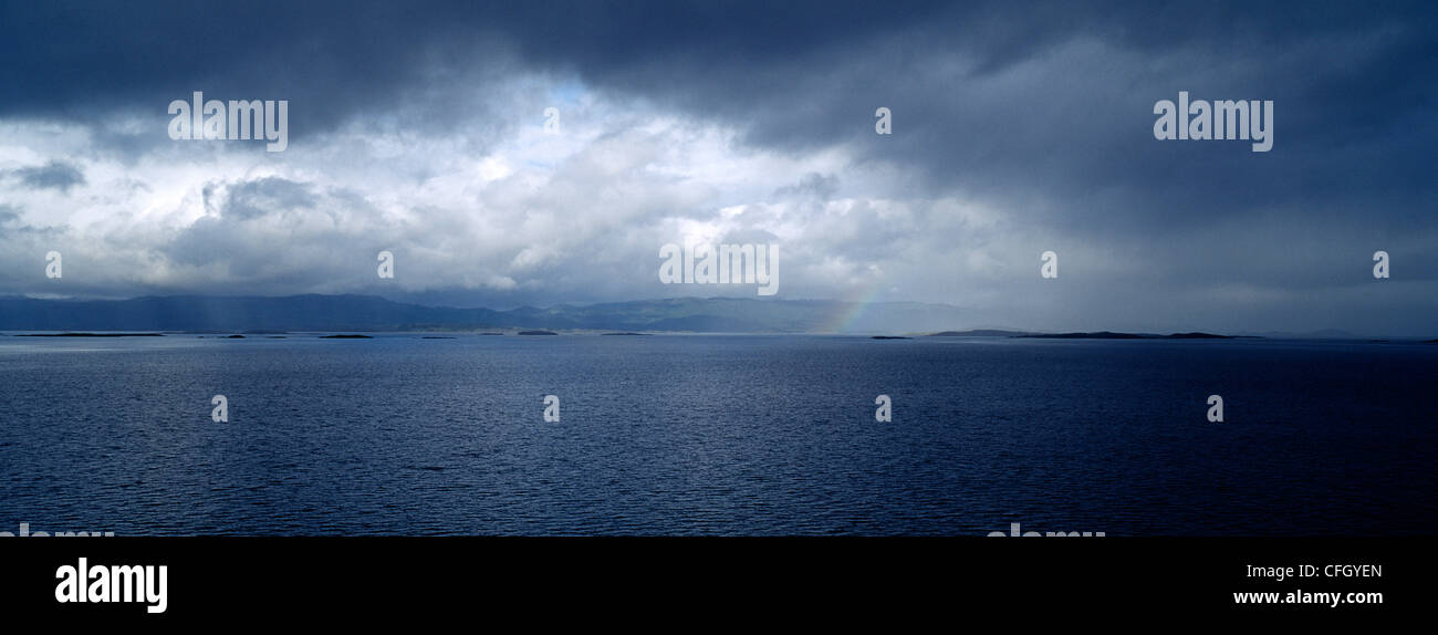 Un arcobaleno discende da una tempesta davanti e temporale su una baia nell'oceano. Foto Stock