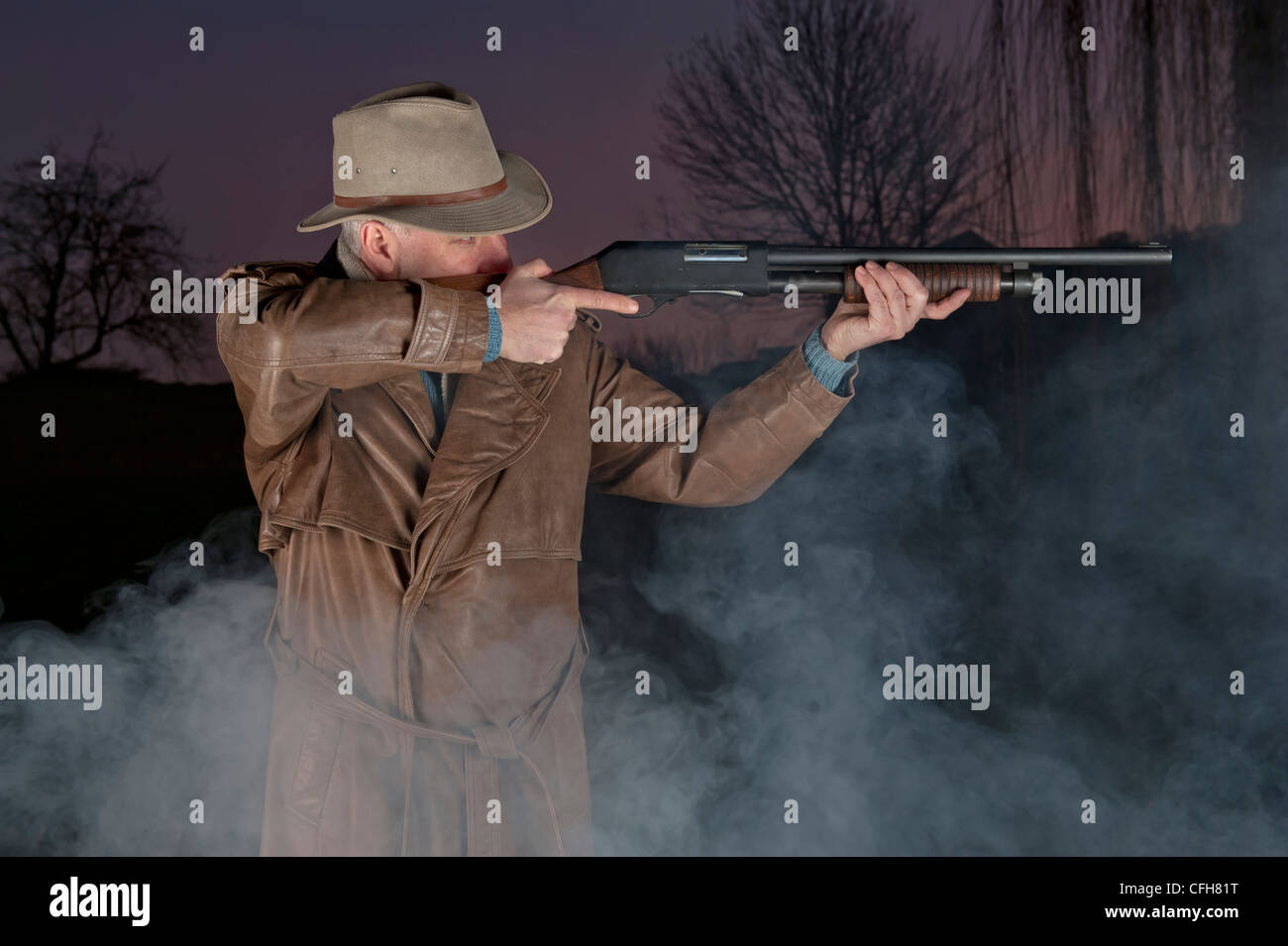 L'uomo con il cappello da cowboy, lungo cappotto di pelle e pistola antisommossa durante la notte Foto Stock