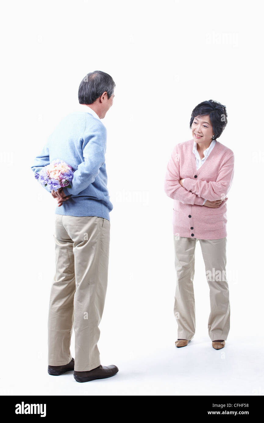 Un uomo anziano come nascondere un mazzo di fiori per una donna anziana Foto Stock