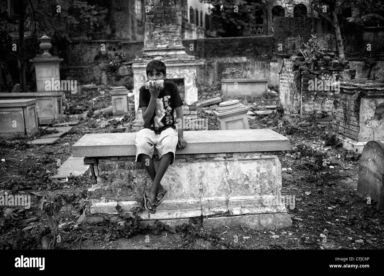 Bambino colla sniffing su una tomba in un cimitero abbandonato a Calcutta, India. Foto Stock