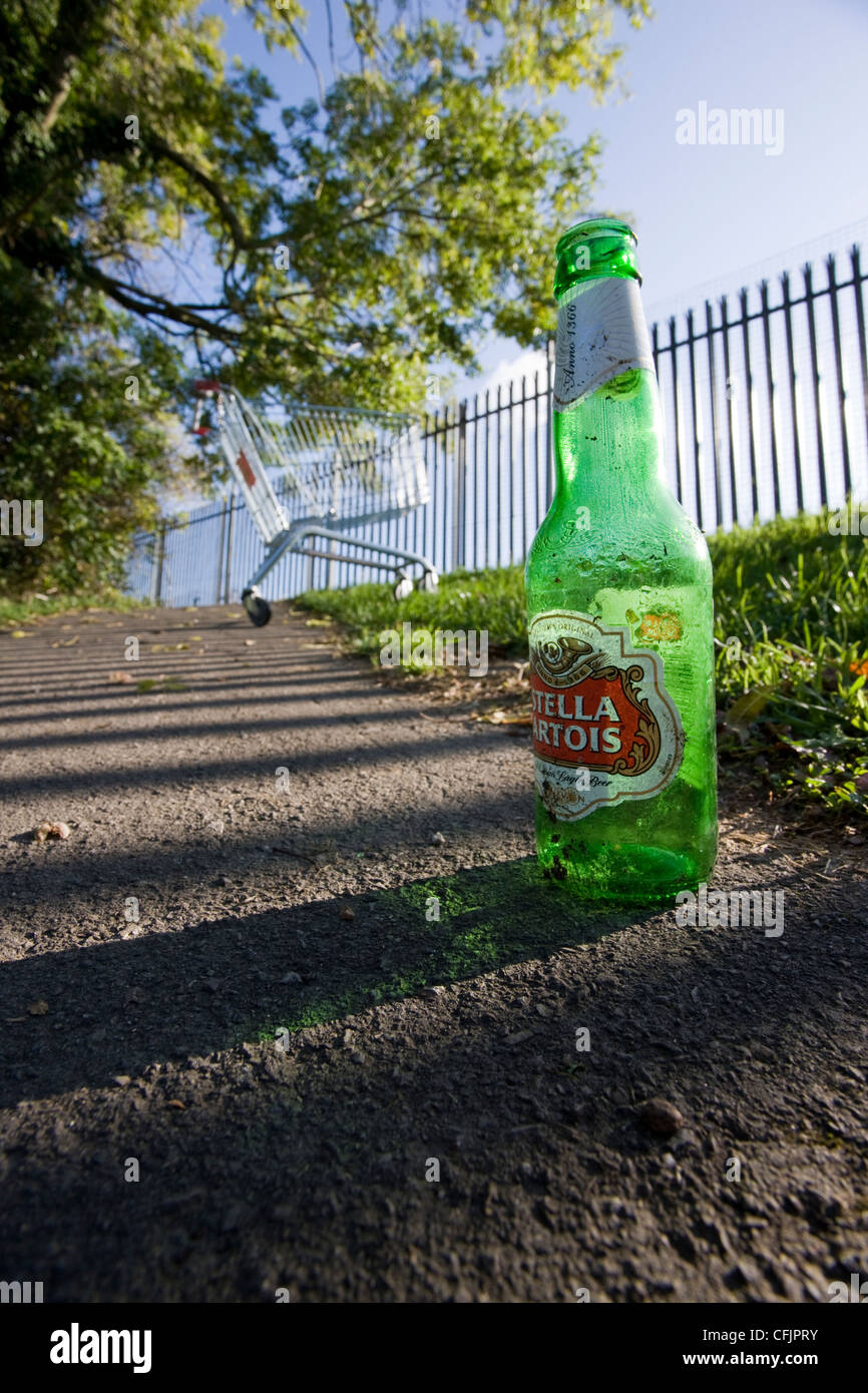 Vuoto bottiglia di birra della Stella Artois brand sul marciapiede con un abbandono carrello di shopping in background Foto Stock