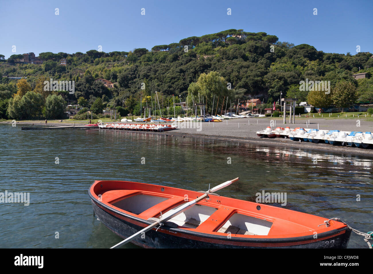 Rosso barca a remi sul lago Albano guardando verso la spiaggia e pedalò Foto Stock