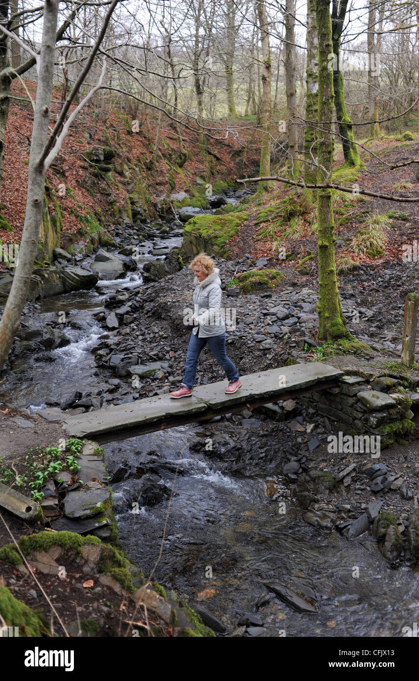 Donna che indossa rosa Timberland boots attraversando un piccolo ponte a piedi nel Lake District Cumbria Regno Unito Foto Stock