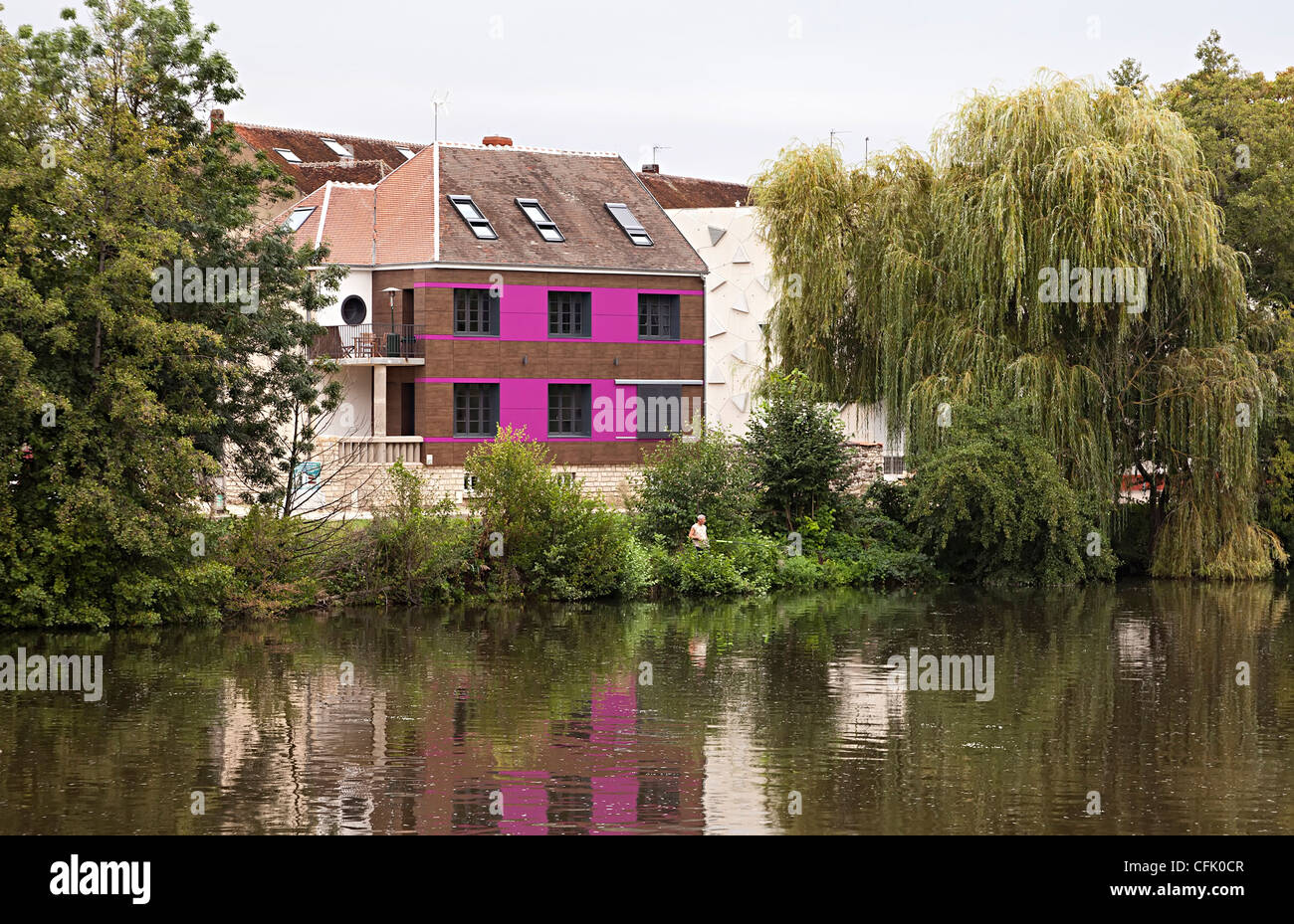 Casa moderna con pareti rosa accanto al fiume con un pescatore in banca, Auxerre, Francia Foto Stock