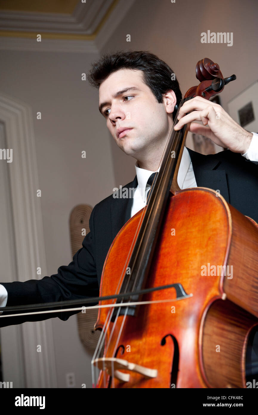 Bel giovane uomo che indossa una tuta e tiranti a suonare il violoncello Foto Stock