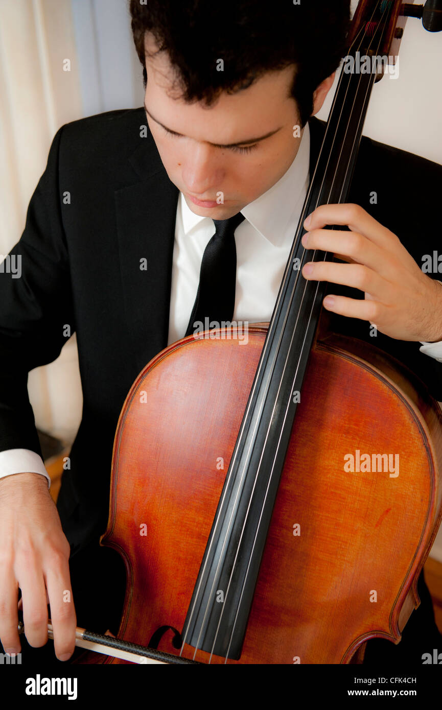 Bel giovane uomo che indossa una tuta e tiranti a suonare il violoncello Foto Stock