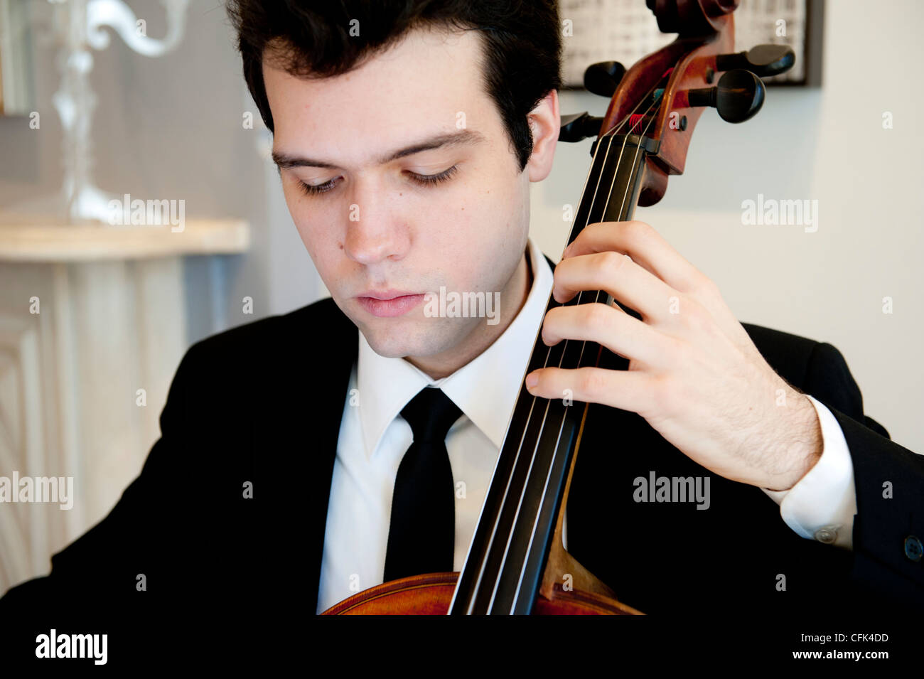 Bel giovane uomo che indossa una tuta e tiranti a suonare il violoncello Foto Stock